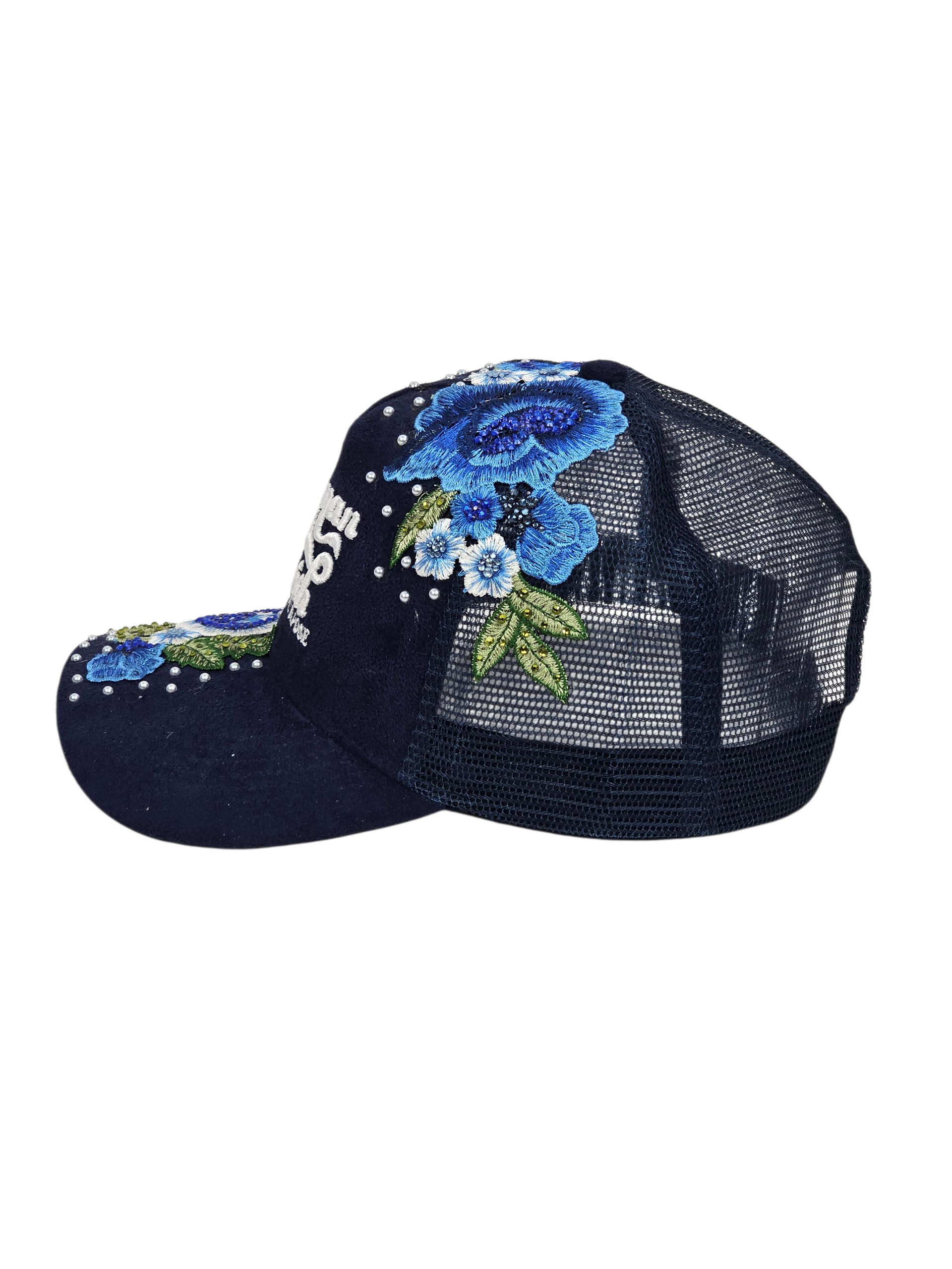 A navy blue trucker-style baseball cap with a mesh back, decorated with blue and white floral embroidery, green leaves, and white rhinestones on the brim and crown.